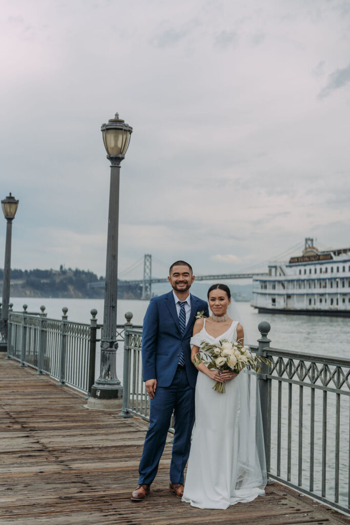 bride and groom on the pier in san francisco with bay bridge and water views in the backdrop