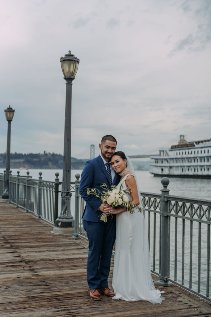 bride and groom on the pier in san francisco with bay bridge and water views in the backdrop