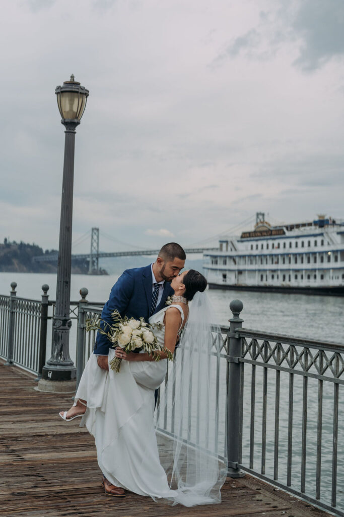 bride and groom on the pier in san francisco with bay bridge and water views in the backdrop